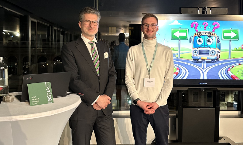 „Zwei Vortragende der Veranstaltung ‚ESG für KMUs‘ von respACT und DORDA stehen vor einem Bildschirm mit einer Comic-Grafik, die eine Entscheidungssituation symbolisiert. Im Vordergrund ein Stehtisch mit respACT-Materialien.“